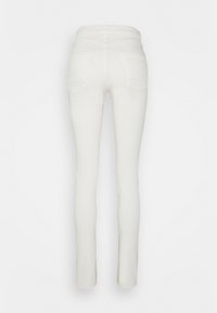 Pantalones de mezclilla blancos de corte slim, con una textura suave, cinco bolsillos y una cinturilla de altura media. Las costuras son visibles en los bolsillos traseros.