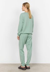 Set di abbigliamento loungewear color verde menta, composto da una felpa dal taglio rilassato e pantaloni della tuta affusolati coordinati. Tessuto morbido con polsini e vita a costine.