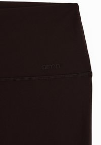 Primer plano de tela negra de tiro alto con costura horizontal visible y pequeño logo en relieve de la marca "aimn".