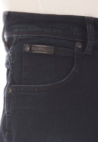 Vaqueros de mezclilla azul oscuro con un diseño clásico de cinco bolsillos, que presentan costuras en contraste y una pequeña etiqueta de marca de cuero negro cerca de la cintura.