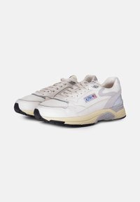 Sneakers bianchi in pelle con accenti in rete, suole beige e dettagli grigi. Presentano lacci e un'etichetta laterale con logo in blu e rosso.