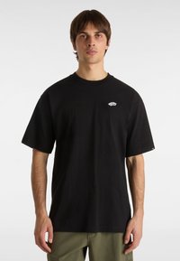 T-shirt in cotone nero con colletto rotondo, maniche corte e un piccolo logo bianco sul petto. Tessuto liscio e vestibilità rilassata.