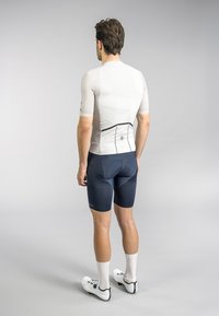 Short-sleeved, light gray athletic shirt with a textured back, paired with dark blue fitted shorts displaying a geometric pattern and white cycling shoes.