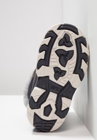 Suela de zapato negra y gris con goma texturizada para tracción. Presenta un patrón de gama profundo, con una entresuela blanca gruesa y bordes reforzados.