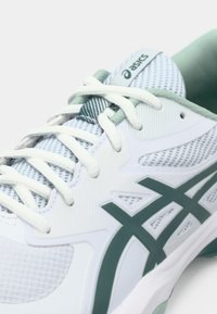 Tênis esportivo branco com parte superior em malha, detalhes em verde e texturizados. Apresenta cadarços brancos e logo da ASICS na língua.
