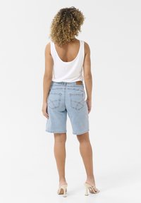 Shorts in denim azzurro chiaro con una vestibilità rilassata, caratterizzati da due tasche posteriori e dettagli cuciti. Indossati con un top bianco a canottiera e tacchi beige.