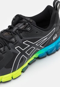 Scarpa da corsa nera con tomaia in mesh, dettagli riflettenti e sistema di ammortizzazione GEL. La suola presenta una sfumatura che va dal verde al blu.