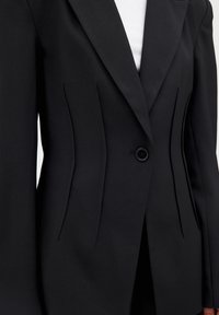 Black tailored blazer featuring a single button closure, structured shoulders, and vertical seam detailing. Made from smooth fabric.