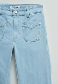 Vaqueros de mezclilla azul claro con cierre frontal de botones, trabillas para cinturón y dos bolsillos delanteros con detalles cosidos.