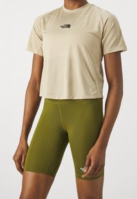 Beige, figursydd t-shirt med kort ärm och logotyp samt gröna cykelshorts. Båda är tillverkade av en slät, stretchig tyg med en elegant design.