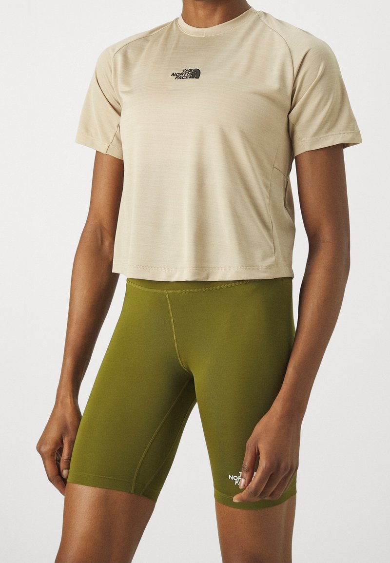 Beige, figursydd t-shirt med kort ärm och logotyp samt gröna cykelshorts. Båda är tillverkade av en slät, stretchig tyg med en elegant design.