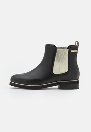 Bottine Chelsea en cuir noir avec un panneau latéral élastique gris texturé, bout rond et petit talon bloc. Comprend un accent métallique et une languette de tirage.