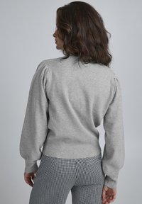 Grå stickad tröja med puffärmar och ribbad fåll, i kombination med svartvita rutiga byxor, som visar en slät textur.