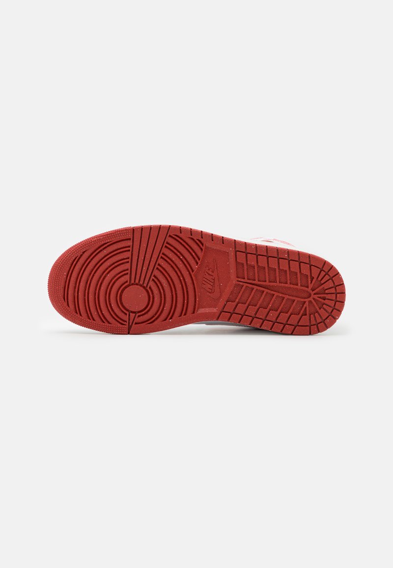 Suela de goma roja con patrones de tracción circulares y lineales; presenta un logo de Nike cerca del talón y una superficie texturizada para mayor agarre.