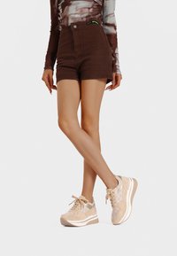 Sneaker in suede beige con dettagli a fantasia, chiusura con lacci e suola bianca spessa. Indossate con pantaloni corti beige a vita alta e una maglietta tie-dye.