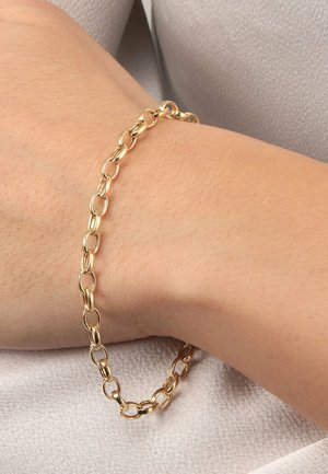 Goldene Kettenarmband mit länglichen, ineinandergreifenden ovalen Formen, das auf einem hellhäutigen Handgelenk liegt, vor einem sanften, reflektierenden Stoffhintergrund.