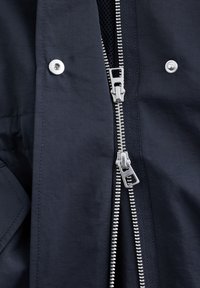 Tamsiai mėlynas švarkelis su sidabriniu užtrauktuku, spaustukais ir tekstūruota pamušalu. Audinys atrodo lygus, matinio blizgesio.