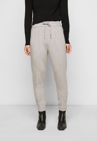 Lichtgrijze sweatpants met een trekkoord in de tailleband, zijzakken en iets taps toelopende pijpen, in combinatie met een zwart aangesloten longsleeve shirt.