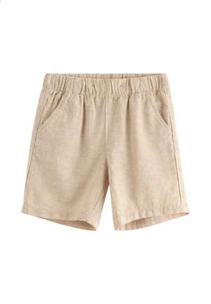 Smilende dreng iført en cremefarvet kortærmet skjorte med grønne palmebladtryk, beige shorts og brune snørebåndssko, stående mod en hvid baggrund.