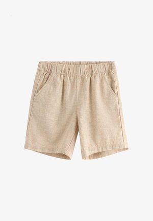 Smilende dreng iført en cremefarvet kortærmet skjorte med grønne palmebladtryk, beige shorts og brune snørebåndssko, stående mod en hvid baggrund.