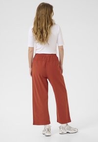 Pantalons amples de couleur rouille avec une taille élastique, associés à un dessus blanc et à des baskets beige clair. Tissu lisse et coupe décontractée.