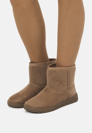 Botas de tobillo de ante marrón con punta redondeada, forro suave y detalles de costura, que cuentan con una suela de goma plana para un mejor agarre.
