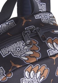 Mochila de tela negra con un diseño de garra en marrón y blanco, con doble cierre de cremallera negra y una superficie texturizada.
