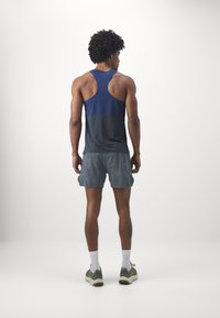 Débardeur de sport en bleu marine et gris, avec une texture lisse et un design à dos nageur. Associé à un short gris, offrant un ajustement confortable.