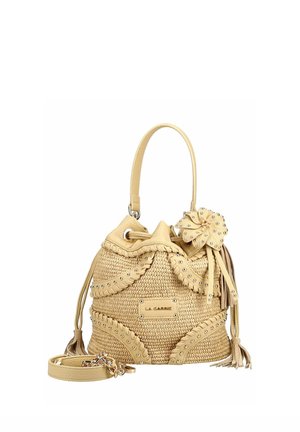 Bolso tipo cubo beige tejido con ribete de cuero tachonado, asa única, borlas decorativas, detalle de flor y correa de hombro desmontable.
