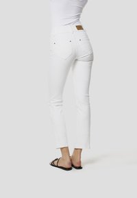 Bílé džíny z denimu s přiléhavým střihem, pasem v polovině výšky a ozdobnou výšivkou na spodní části nohavic; kombinované s černými sandály na pásky.