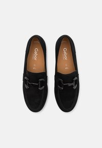 Mocassins en daim noir avec une boucle décorative, une semelle intérieure en cuir et des coutures contrastées. Conçus pour le confort avec un bout arrondi.