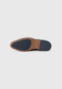 Suela de zapato de cuero azul marino con un patrón de agarre de goma texturizada, que presenta un distintivo diseño de diamante diagonal y un borde contrastante en color beige.