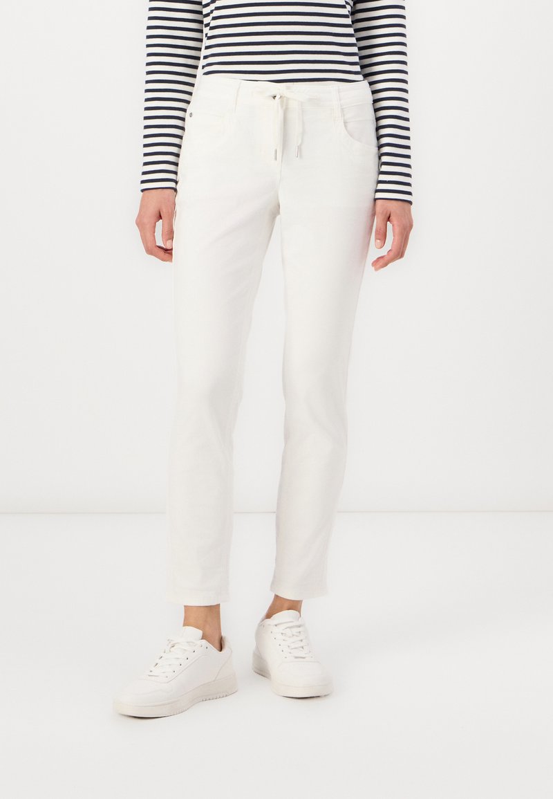 Hvite bomullsbukser med en avsmalnet design, med snor i livet, frontlommer, og iført hvite sneakers og en stripete topp.