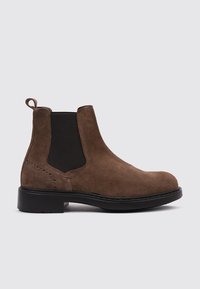 Botín Chelsea de ante marrón con paneles laterales elásticos, tirador y suela de goma negra. Presenta perforaciones decorativas en el lateral.