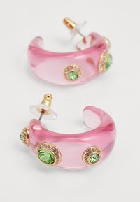 Rosa durchsichtige Creolen mit goldenen Akzenten, die auf einer Seite mit grünen und rosa Edelsteinen verziert sind, um zusätzliche Details zu bieten.