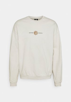 Vaalea beige huppari, jossa on pyöreä pääntie, ribatut hihat ja helma, painettu aurinkografiikka sekä teksti "KAOTIKO SOCIETY."