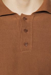Polo shirt marrone in maglia caratterizzato da un tessuto testurizzato, tre bottoni marroni al colletto e un design del colletto classico.
