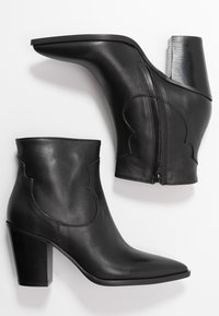 Par de botas de cuero negro hasta el tobillo con punteras afiladas, tacones cuadrados, cremalleras laterales y costuras decorativas en los lados exteriores.