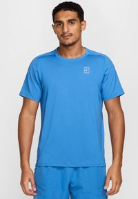 Maglietta sportiva a maniche corte di colore blu brillante, realizzata in tessuto traspirante. Presenta un colletto rotondo e un piccolo logo bianco sul petto.