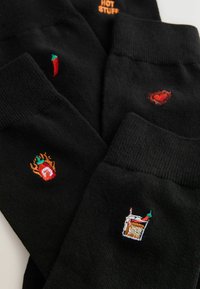 Schwarze Socken mit kleinen Stickereien: Chilischote, Flasche mit feuriger scharfer Soße, Herz und ein Getränk mit Strohhalm und Chilischote.
