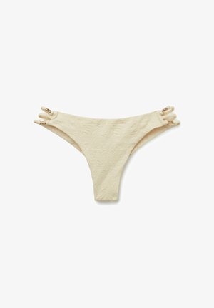 Parte inferior de bikini beige texturizada con triples tiras laterales que cuentan con pequeños detalles de anillos dorados sobre un fondo blanco.
