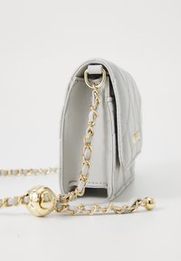Borsa trapuntata grigia con tracolla in catena tono oro e hardware decorativo rotondo. Presenta una forma rettangolare e una texture in pelle morbida.