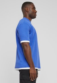 T-shirt en coton bleu à manches courtes, avec des bordures blanches sur les manches et l'ourlet. Le tee-shirt a une coupe décontractée et un col rond.
