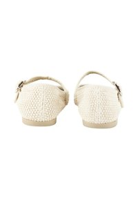 Zapatos de tela beige tipo slip-on con un acabado texturizado, que cuentan con una correa trasera y un pequeño detalle de hebilla plateada. Suelas de goma planas.