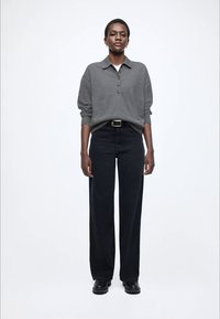 Szary sweter polo z dzianiny z detalami na guziki, zestawiony z czarnymi, szerokimi spodniami z wysokim stanem oraz masywnymi czarnymi botkami.