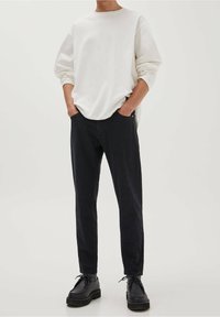 Sudadera blanca de manga larga con hombros caídos, combinada con pantalones ajustados azul marino oscuro. Zapatos negros con cordones y suela gruesa.