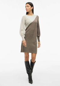 Abito a maglia con un design a blocchi di colore beige e marrone, maniche lunghe con dettagli a palloncino e una silhouette dritta che termina sopra il ginocchio.