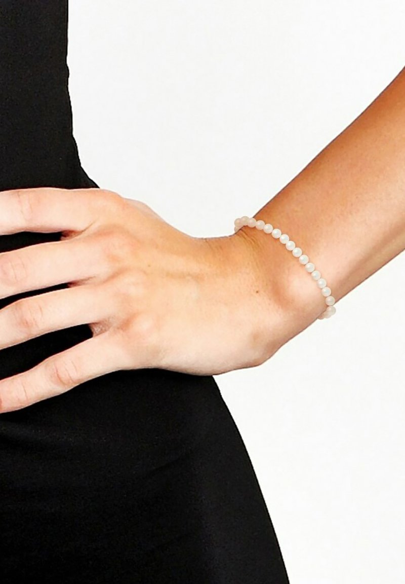 Bracelet en perles composé de petites perles rondes blanches translucides sur un poignet, présenté sur un fond de vêtement noir.