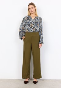 Camicia a fantasia blu, crema e oro; vestibilità rilassata. Pantaloni a gamba larga verde oliva con vita alta; tessuto con trama. Tacchi marroni.