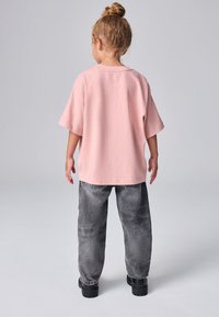 Vaaleanpunainen puuvillainen t-paita, jossa on lyhyet hihat, yhdistettynä löysiin harmaisiin farkkuihin. Asu on yksinkertainen ja rento.